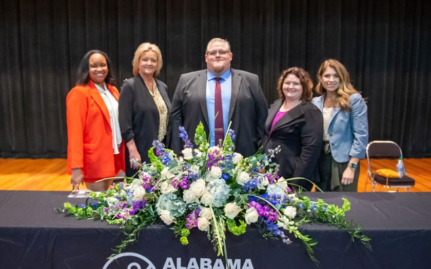Five staff members smiling before a table of flowers