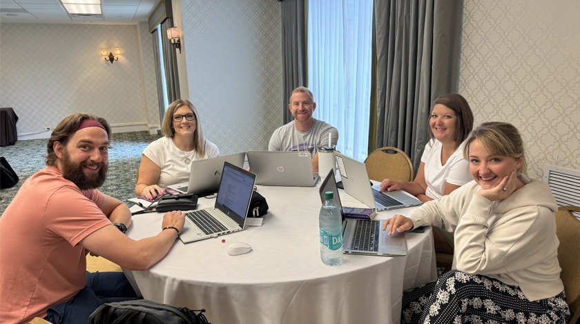 Five staff members sitting together at a round table with their laptops open