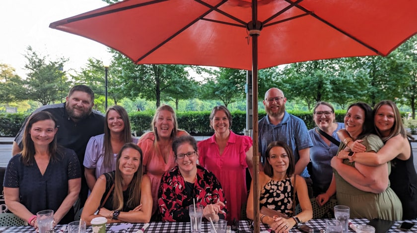Staff gathered together and sitting under an umbrella