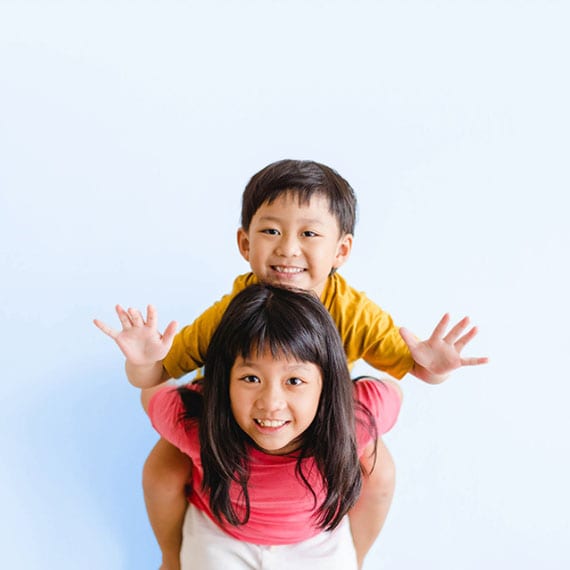 Young student in a lime green sweater and pink headphones jumping with her arms raised in front of a blue wall