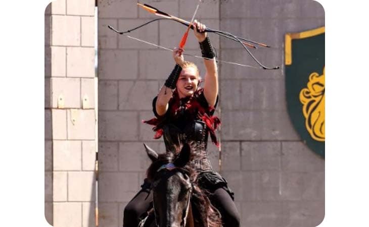 Image of Brenna on her horse doing a stunt with her bow and arrow. 