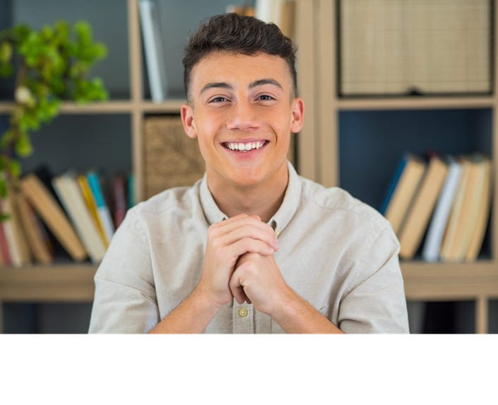 College age male looking at the camera for a portrait with books  in a shelf in backdrop