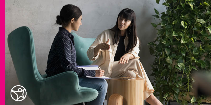 Two professional women sitting in chairs and engaged in a conversation