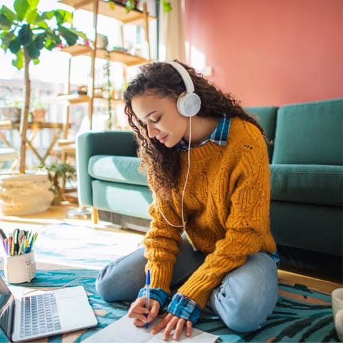 A person wearing an orange sweater working on the floor near a sofa and her laptop. 