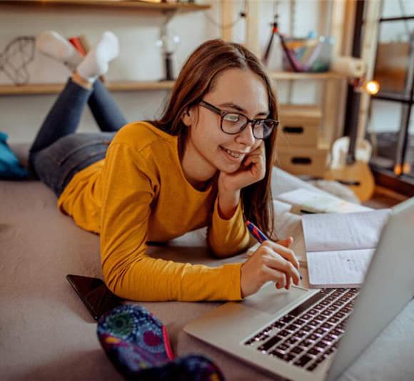 Connections Academy Student wearing a yellow shirt taking notes on her notebook in her room