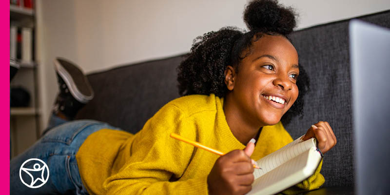 Connections Academy student holding a pencil and notebook and looking at her laptop. 