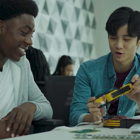 Two people sitting at a table working with electronic components.